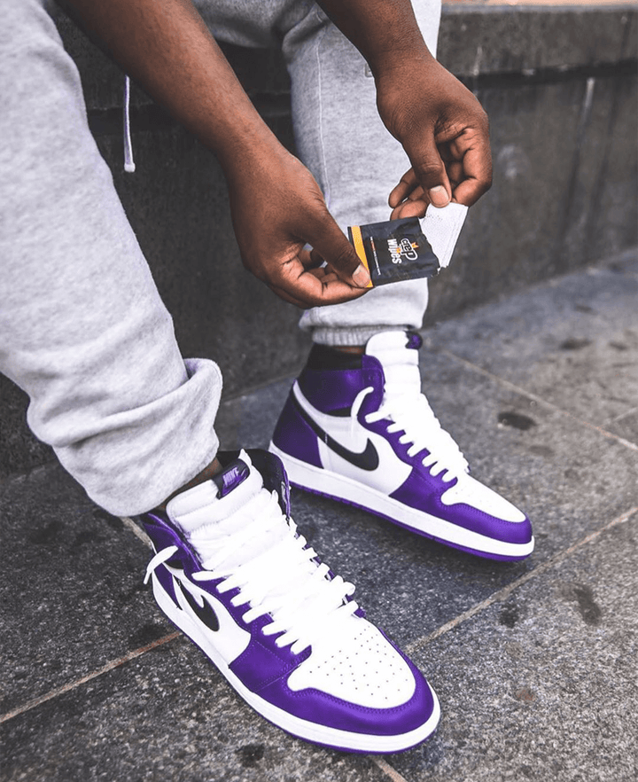 Man wearing purple Nike sneakers opening a pack of cleaning wipes